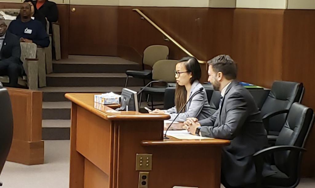 Two people, Annie Tran and Casey Helbling, speak at a podium at the state capitol.