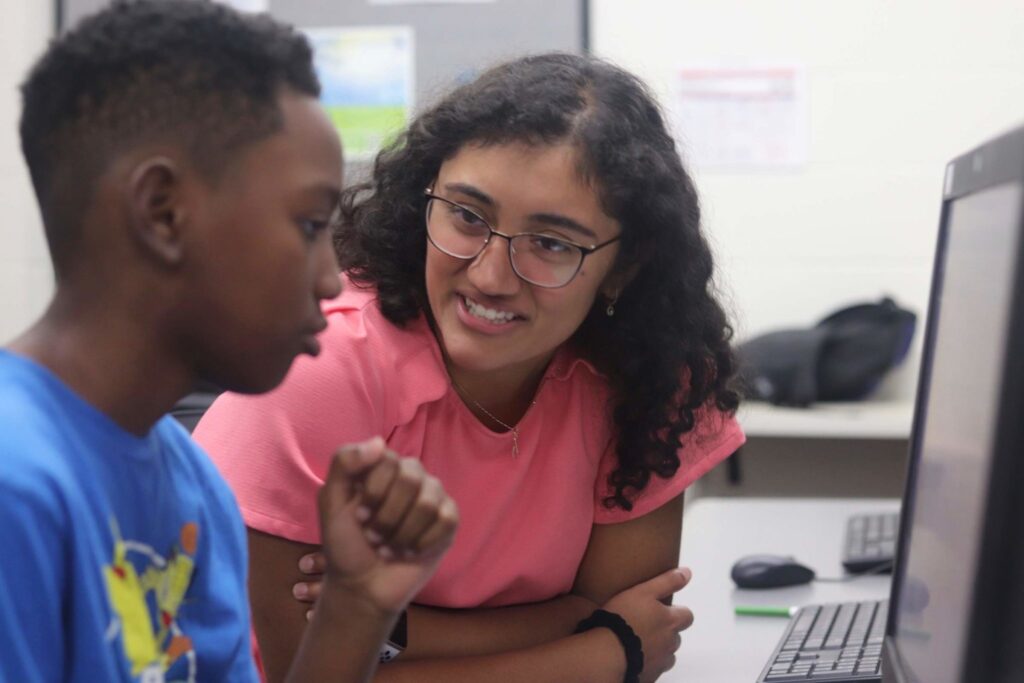 A young child and a young woman talking while looking at a computer screen together.