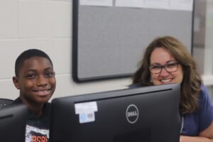 An adult and a child smile at the camera while working on a computer.